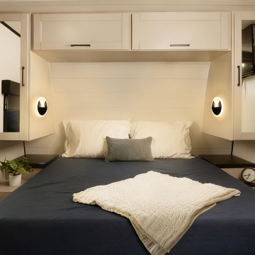 Cozy bedroom with a neatly made bed featuring white pillows, a gray decorative pillow, and a textured white blanket, surrounded by modern light fixtures and minimalistic decor.