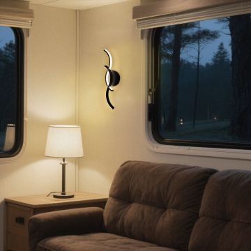 A cozy living room scene featuring a modern wall sconce, a table lamp on a wooden side table, and a brown upholstered sofa, set against a backdrop of large windows with a view of trees outside during twilight.