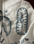 The hoodie looks very good, the quality is very good. The Bape bag, the Bape tag, the bullseye sign, the bullseye sign is also printed on very good, the stitching, the shark face, the WGM (World Gone Mad) is printed on good. Even the white Color is right and the wrist sleeves also have a perfect white color But the most crazy thing about this hoodie is that it even glows when the hoodie is in a dark area like the real one, you only have to put the hoodie in a light area or put the hoodie right under a lamp, so the material that glows can charge up on light. This feature is just so crazy. I would also consider sizing up if you want a more baggy look and if you want to zip up your hoodie completely to the top. Overall the hoodie is very good and PkStockX is a very customer friendly company and I can only recommend them, their work is just insane. I will also buy again from here in the future. Thank you so much PkStockX.