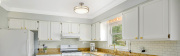 A modern kitchen featuring white cabinets, a granite countertop, and stainless steel appliances, illuminated by a stylish ceiling light and natural light from a nearby window.