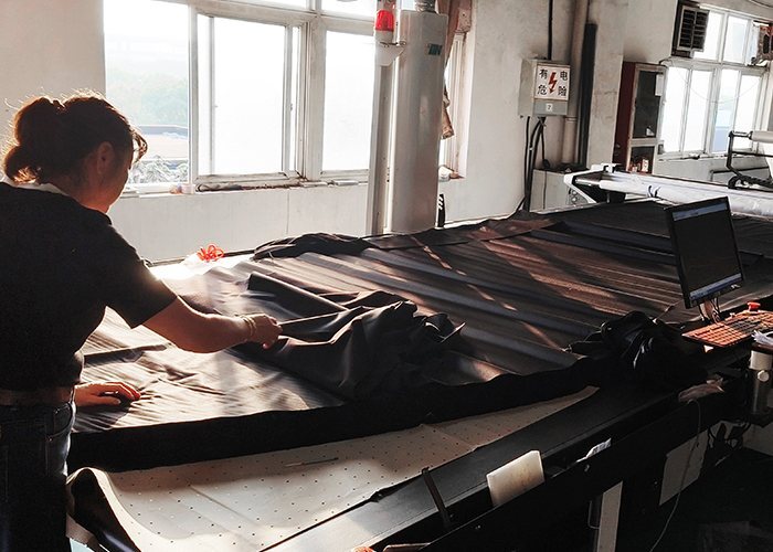 Operator spreading cover fabric on an in-house cutting table at the JK Covers factory