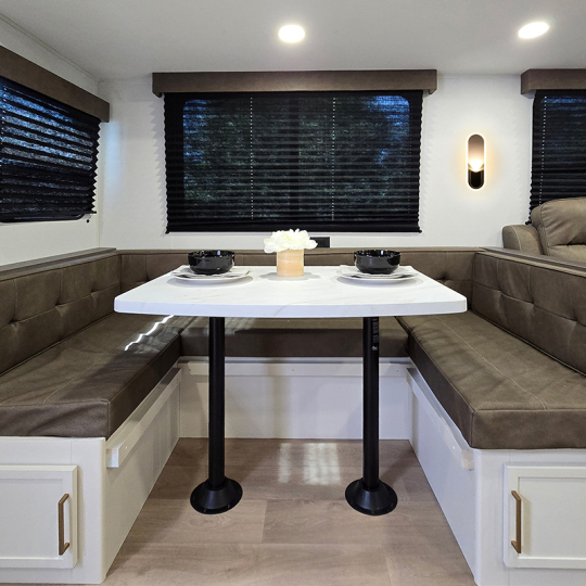 A modern cozy dining area featuring a white table with two black bowls, surrounded by brown upholstered benches and illuminated by wall sconces, creating a warm atmosphere.
