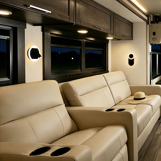A modern living space featuring two light-colored leather sofas with built-in cup holders, illuminated by ambient light from wall fixtures and large windows, creating a cozy atmosphere. A straw hat rests on one sofa, complementing the evening setting.